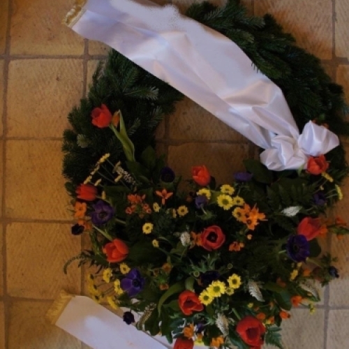 Begravelseskrans med farverige blomster og gran med bånd