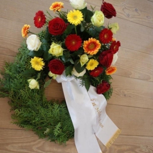 Begravelseskrans med farverige blomster og gran med bånd