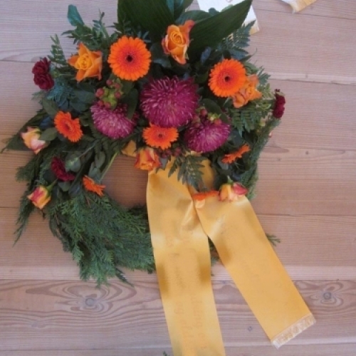 Begravelseskrans med orange og lilla blomster med gult bånd