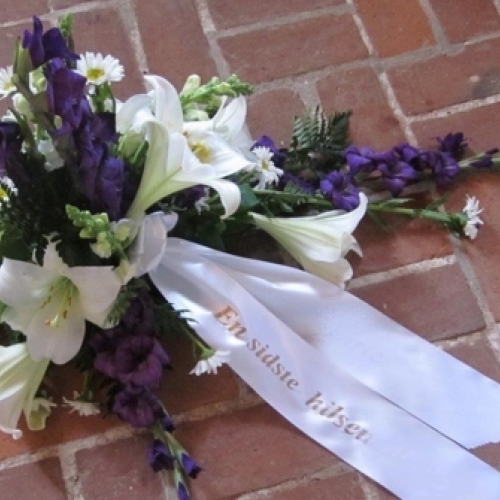 Bårebuket med hvide liljer, lilla blomster og bånd med tekst