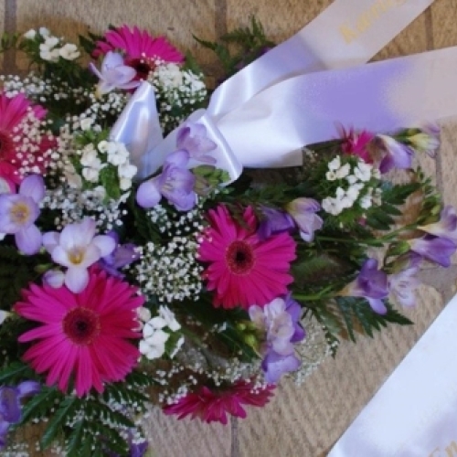 Bårebuket med pink gerbera, lilla blomster og hvidt bånd