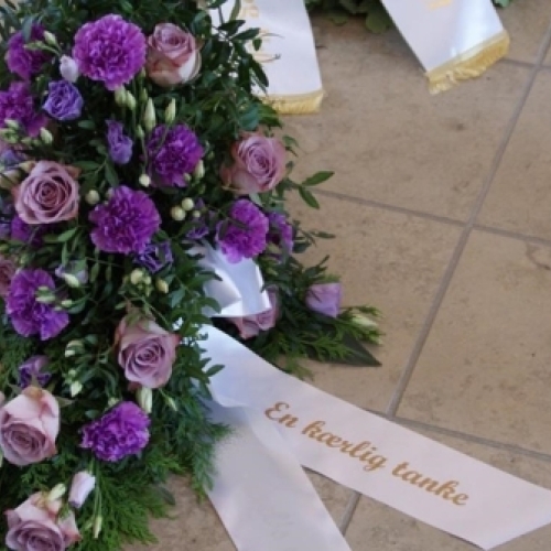 Begravelseskrans med lilla roser, lilla blomster og hvidt bånd