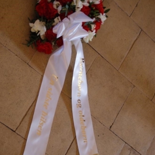 Begravelseskrans med røde og hvide blomster og hvidt bånd