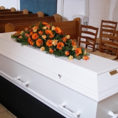 Kistepynt med gule og hvide blomster arrangeret på kiste i kirkerum