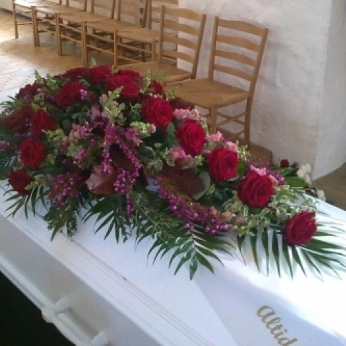 Kistepynt med lyserøde roser og hvide nelliker arrangeret på hvid kiste til begravelse