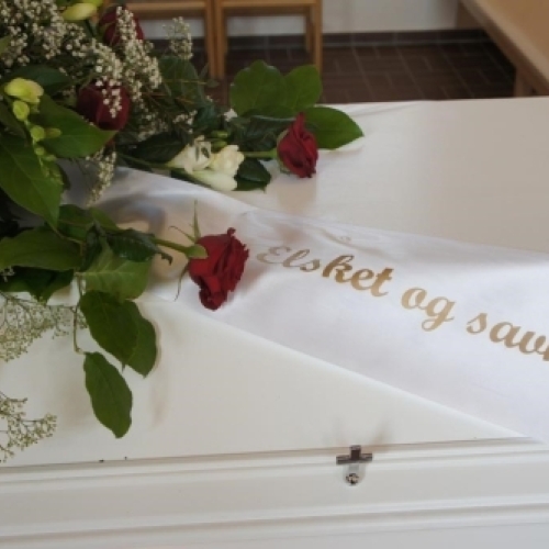 Kistepynt med røde og hvide roser samt mindebånd på hvid kiste