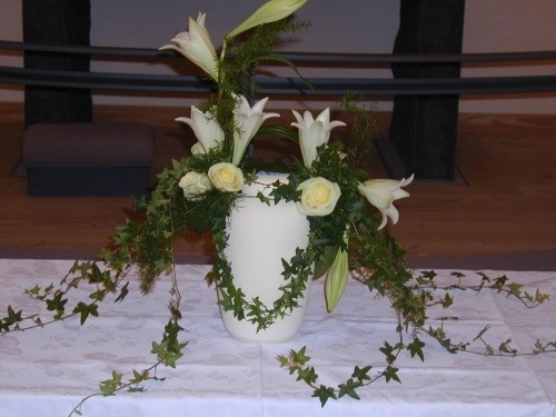Urne med blomster på bordeaux dug foran alter i kirke ved bisættelse