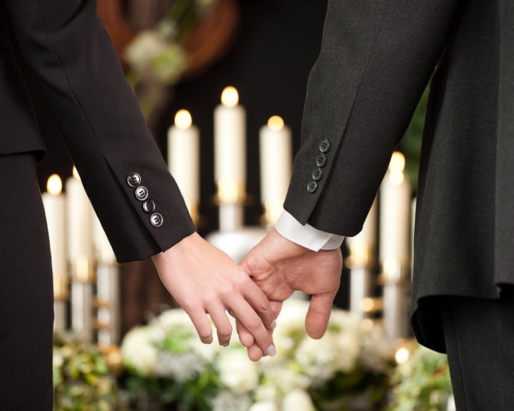 Pårørende holder i hånd under begravelse arrangeret af lokal bedemand.