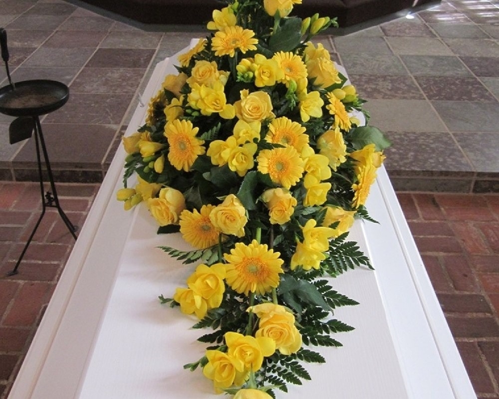 Kistedekoration med gule blomster til begravelse og bisættelse.